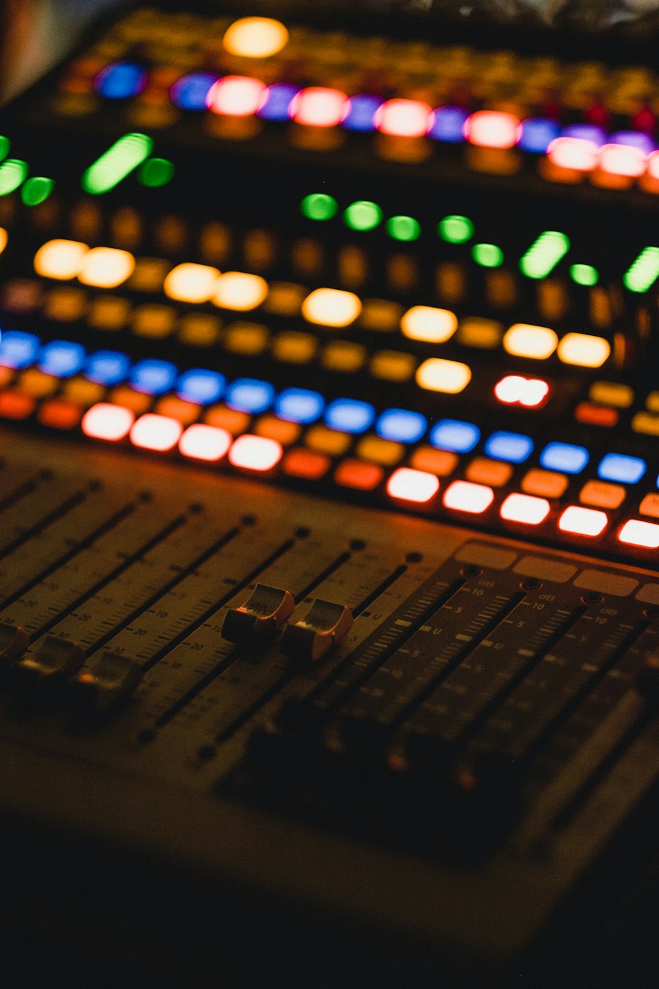Console di missaggio audio con pulsanti e fader illuminati.
